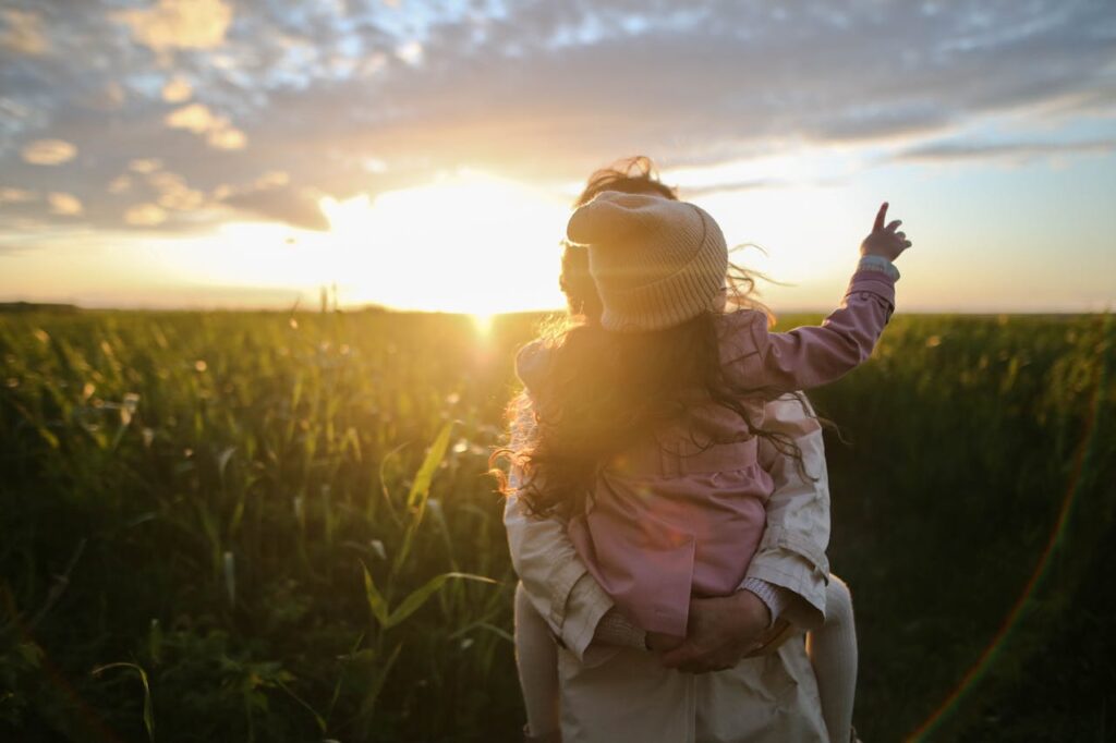 pexels photo 1683975 A mother and daughter embrace and point at the sunset in a grassy field.